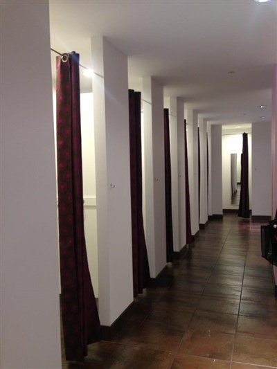 A hallway in a clothing store with fitting rooms featuring dark curtains and a wooden floor.