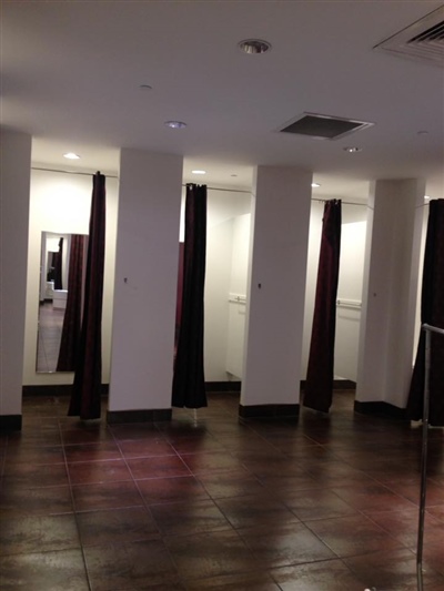 A fitting room area in a clothing store with multiple stalls, each featuring dark curtains, and a wooden floor.