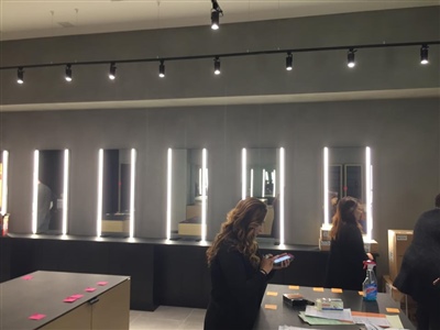 A modern retail store interior with illuminated mirrors on the wall, track lighting on the ceiling, and people working at a counter.