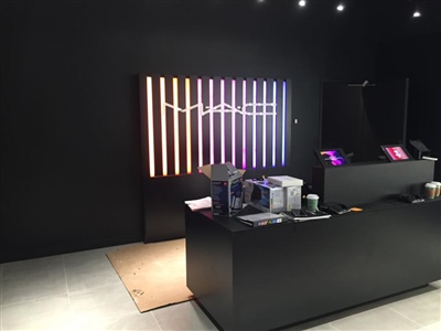 A sleek retail store interior with a black counter, a wall display of colorful vertical lights, and various electronic equipment on the counter.