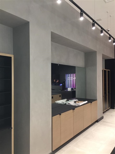 A modern retail store interior with gray walls, black countertops, wooden cabinets, and overhead track lighting.