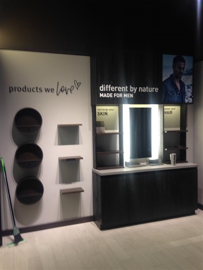 A retail display area featuring shelves and a lighted mirror, with signs that read "products we love" and "different by nature."