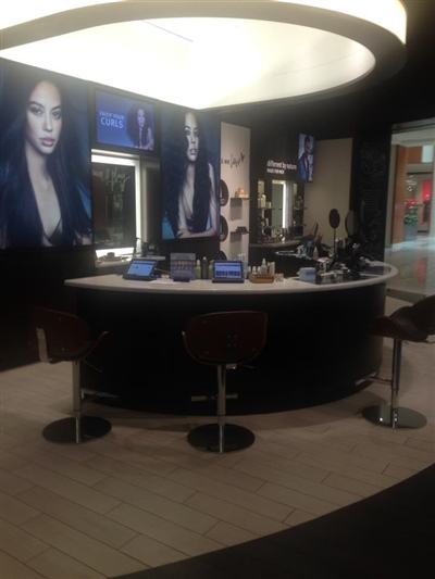 A modern salon setup with a circular counter, high stools, and large promotional images of models with sleek hairstyles on the walls.