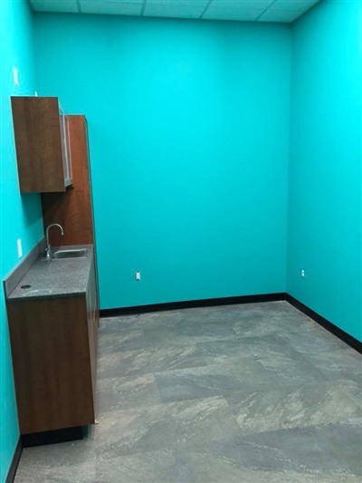 A small room with bright turquoise walls, a gray tile floor, and a wooden cabinet with a sink.