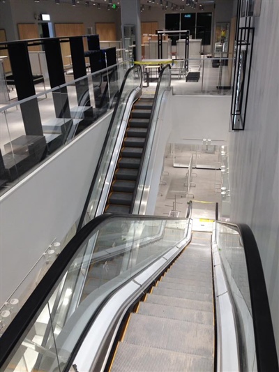 A modern interior with escalators leading to different floors, surrounded by glass railings and minimalistic decor.