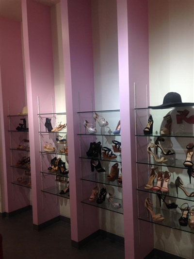 A shoe store display with glass shelves showcasing various styles of women's footwear, set against light pink columns.