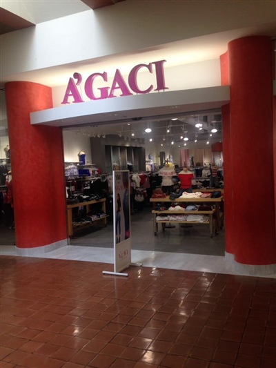 The entrance to an A'GACI store in a mall, featuring red columns and a brightly lit interior displaying various clothing items.