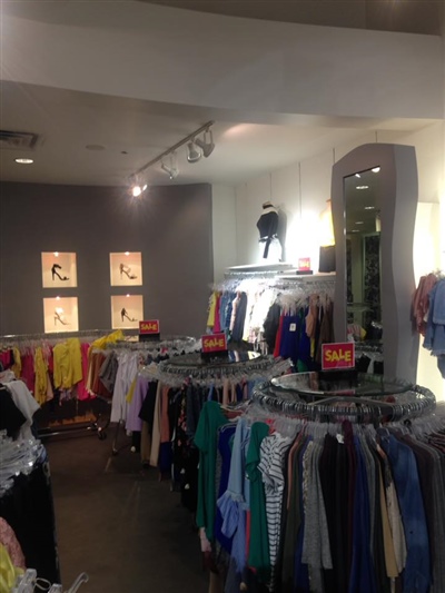 A clothing store interior with racks of colorful garments, sale signs, and a wall display with framed pictures and mannequins.