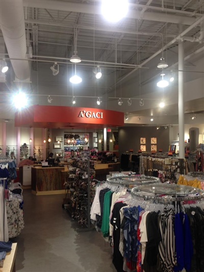 A clothing store interior with racks of various garments and a prominent red A'GACI sign hanging above the entrance area.