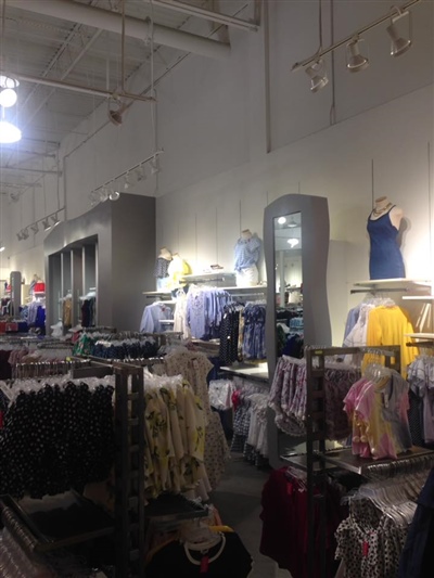 A clothing store interior with racks of colorful garments, mannequins on top shelves, and bright overhead lighting.