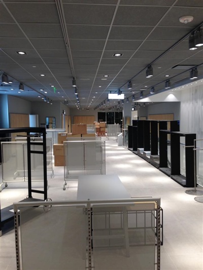 An empty retail store interior with numerous display racks, modern lighting, and some cardboard boxes in the background.