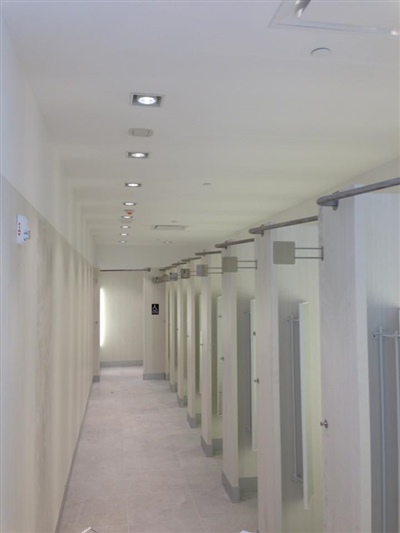 A long corridor with clean, modern restroom stalls on both sides and ceiling lights above.