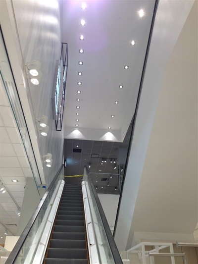 An upward view of an escalator leading to the next floor, surrounded by a modern, brightly lit interior.