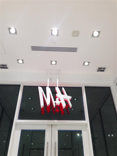 The entrance of an H&M store with a large red logo hanging from the ceiling, surrounded by bright ceiling lights.