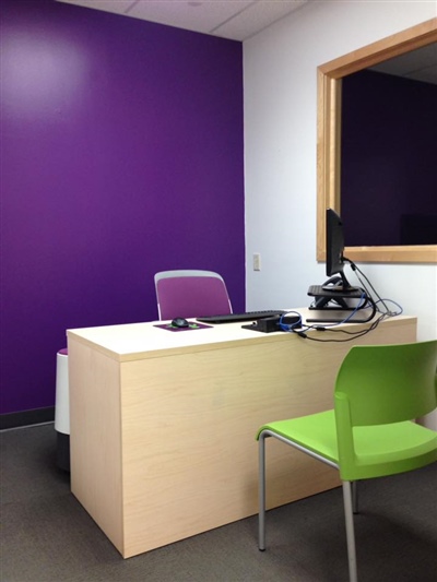 A small office with a desk, green chair, computer setup, and a purple accent wall.