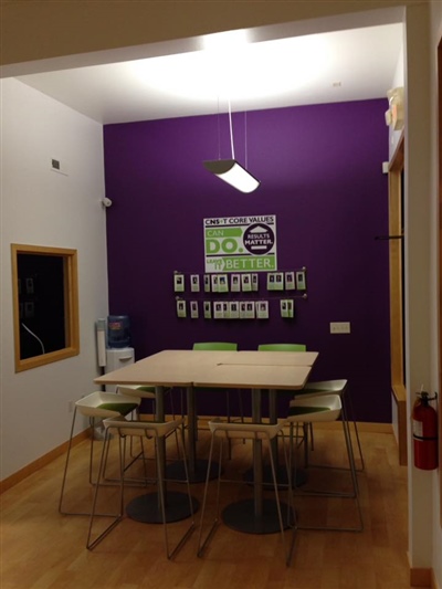 A cozy meeting area with a table, chairs, a purple accent wall, and a display of photos and notes on the wall.