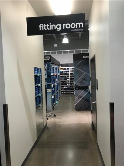 A hallway leading to the fitting room area, with shelves of clothing visible in the background and a "fitting room" sign above.