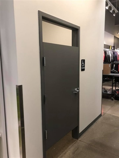 A gray door in a retail store, leading to a fitting room, with clothing racks visible in the background.