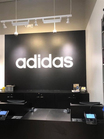 The checkout area of an adidas store, featuring a prominent black wall with the white adidas logo and cash registers below.