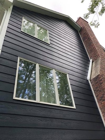 A tall, modern house exterior with dark siding and white-trimmed windows, viewed from below, adjacent to a brick chimney.