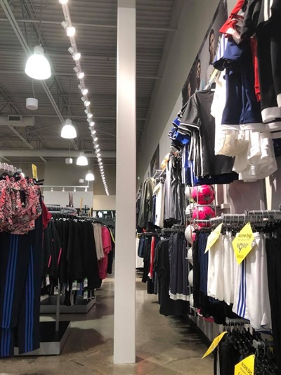 A retail store aisle with racks of clothing and accessories on both sides, illuminated by overhead lights.