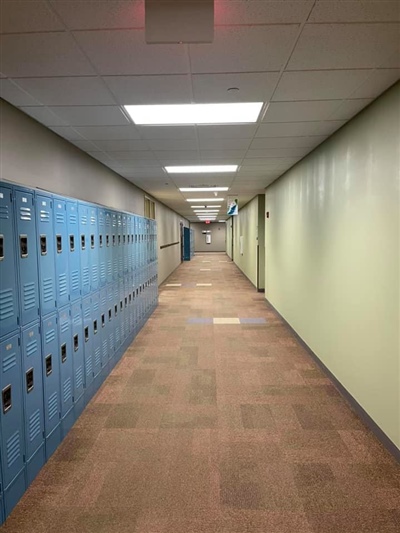 A long, empty school hallway with blue lockers on one side and cream-colored walls, lit by ceiling lights.