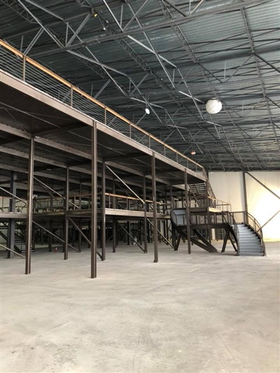 A large, empty industrial warehouse with high ceilings, metal beams, and a multi-level structure with metal stairs.