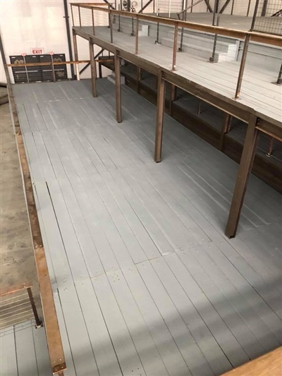 A view of an empty industrial warehouse mezzanine with gray wooden flooring and metal support beams.