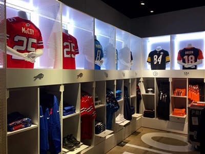 A retail display area showcasing sports jerseys and gear, with illuminated shelves and various team uniforms.