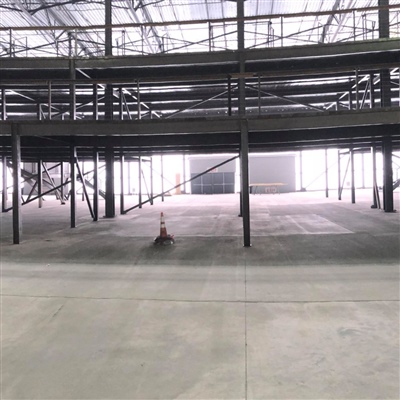 A spacious, empty industrial warehouse with metal beams, a high ceiling, and a traffic cone on the concrete floor.