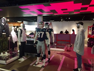 A retail store display featuring mannequins dressed in various sports apparel, including a football uniform, under bright pink ceiling lights.