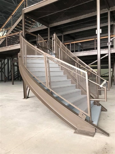 A set of metal stairs with railings in an empty industrial warehouse, leading to a mezzanine level.