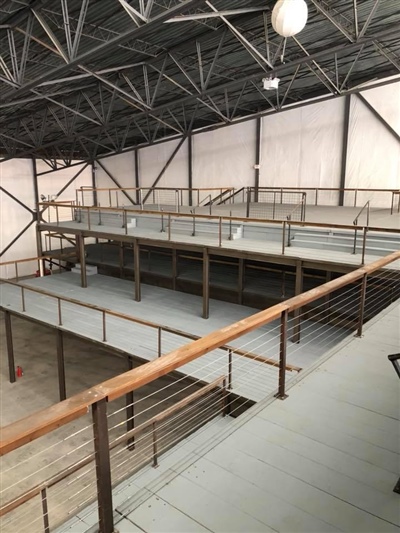 An empty industrial warehouse with metal beams, multiple mezzanine levels, and wooden railings.