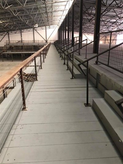 A walkway with metal railings in an empty industrial warehouse, extending along a mezzanine level.