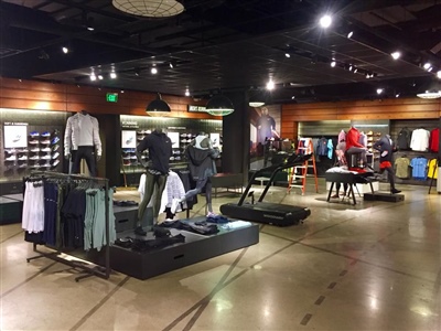 A retail store interior with mannequins displaying sports apparel, clothing racks, and shelves, illuminated by dim overhead lighting.