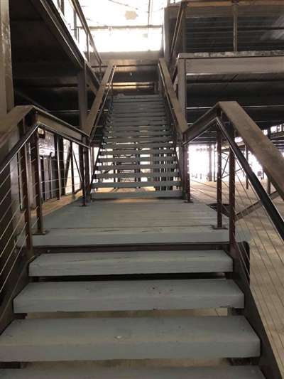 A set of metal stairs with railings in an empty industrial warehouse, leading to an upper mezzanine level.