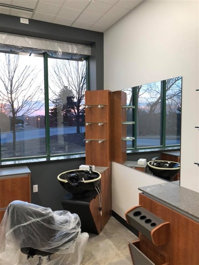 A modern hair salon corner with a washing station, large mirrors, wooden cabinets, and a window offering a view of the outside.