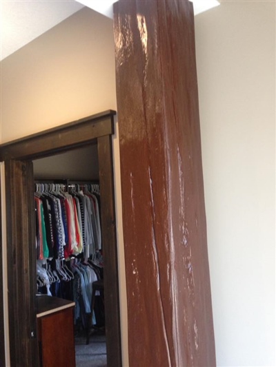 A closet with hanging clothes, a brown wrapped support column, and beige walls.