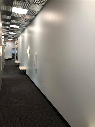 A long hallway with white walls, carpeted flooring, and ceiling lights, leading to other rooms in an office or commercial building.