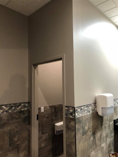 A restroom with tiled walls, a doorway leading to another area, and a wall-mounted paper towel dispenser.