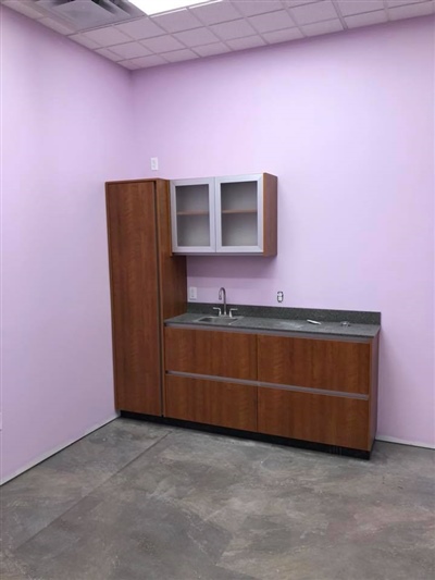 A small room with pink walls, featuring a wooden cabinet and countertop with a sink, and concrete flooring.