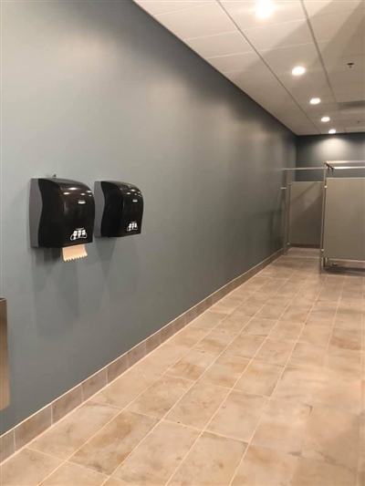 A clean restroom with blue walls, tiled flooring, wall-mounted hand dryers, and toilet stalls in the background.