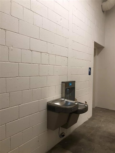 A water fountain and bottle filling station mounted on a white brick wall in a hallway.