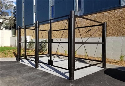 A metal structure with open sides, likely for bicycle storage, situated on a concrete pad near a modern building.