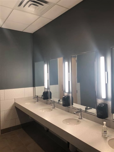 A modern restroom with a long countertop featuring multiple sinks, large mirrors with vertical lights, and a dark gray wall.