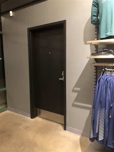 A black door in a retail store, with clothing displayed on shelves nearby and a concrete floor.