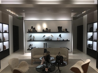 A stylish retail store interior with illuminated shelves displaying shoes and handbags, modern seating, and elegant decor.