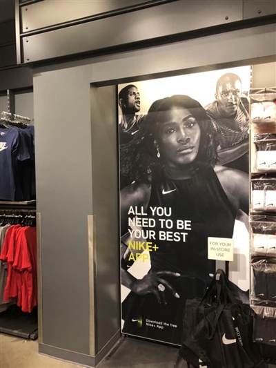 A retail store display featuring a large Nike advertisement with an athlete and the slogan "All You Need to Be Your Best," surrounded by racks of clothing.