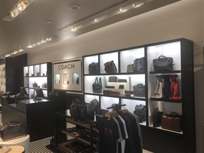 A luxurious retail store interior featuring illuminated shelves displaying Coach handbags and accessories, with modern furnishings and elegant lighting.