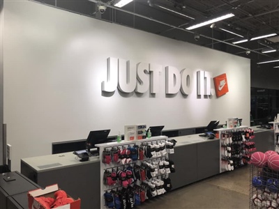 A Nike store checkout area with a large "Just Do It" slogan on the wall, cash registers, and racks of accessories and merchandise.